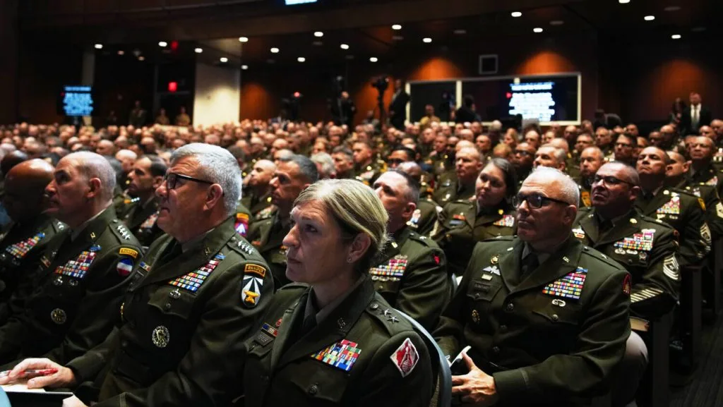 Trump and Hegseth speaking at a meeting in the auditorium of the Naval Academy. blond white woman looking forward with hundreds of other Generals behind her