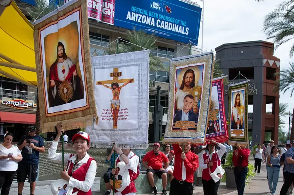 people dressed in MAGA red and white outfits. holding sings of Jesus and charlie Kirks face together
