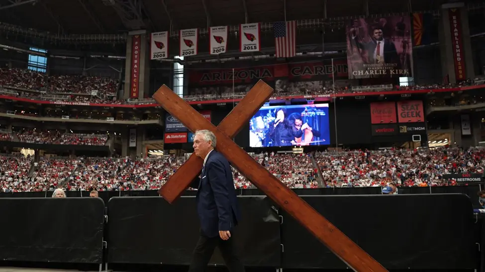 Man carrying giant cross on procession through the floor of charlie kirks Funeral