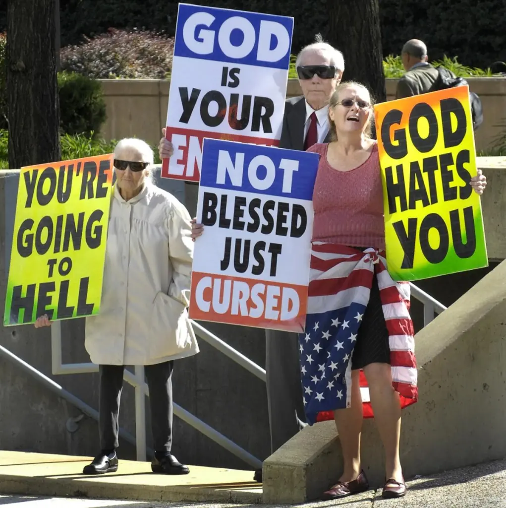 Westboro Baptist Church members holding signs condemning people to hell. "You're Going to Hell "God Is Your Enemy" "Not Blessed Just Cursed" "God Hates You"